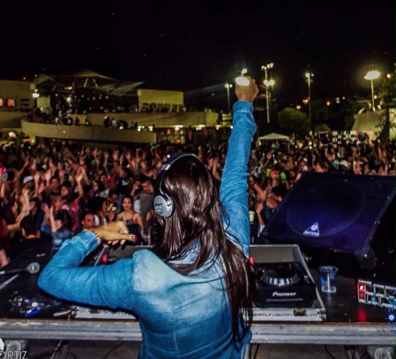 DJ Thaa de costas no palco, com o braço levantado diante do público